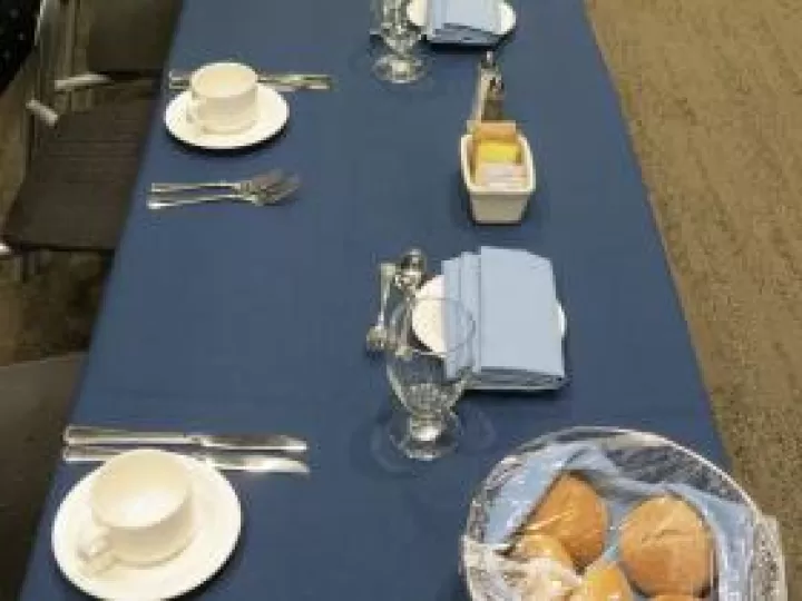 A table set with utensils, napkins, coffee cups, and dinner rolls