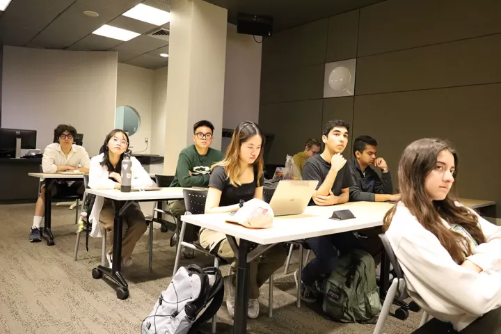Students in a course sitting at tables and listening to a speaker