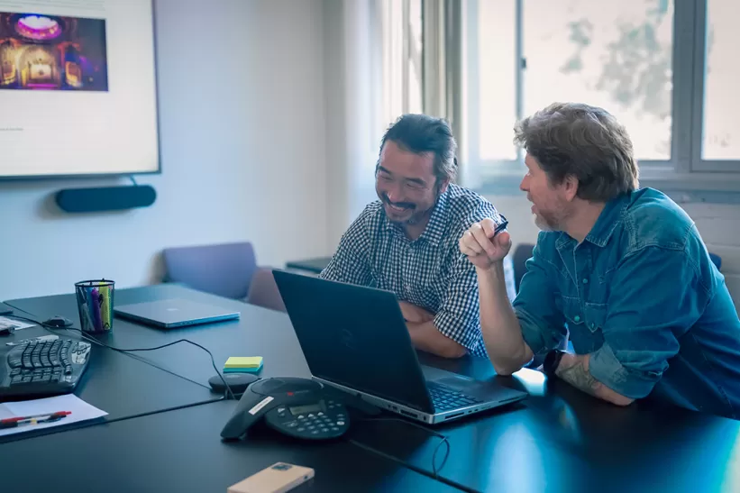 Two men talking at a table with a laptop in front of them