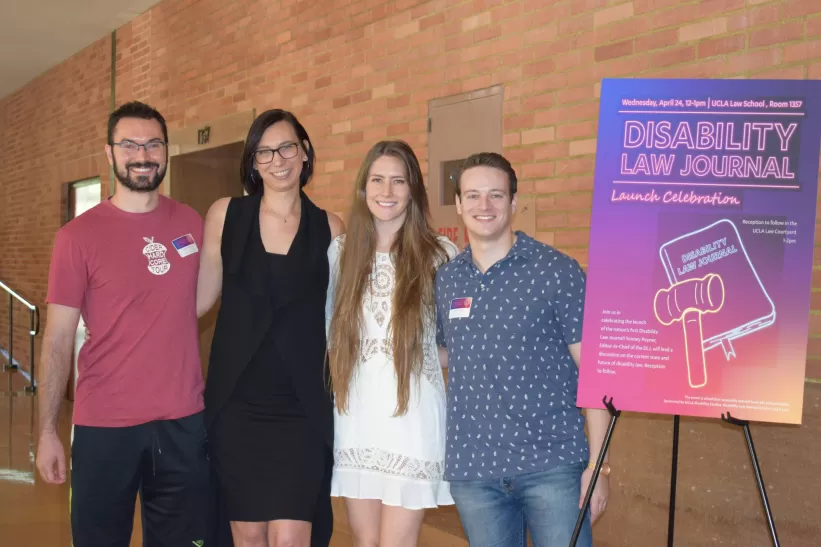 Four UCLA Law students standing next to the Disability Law Journal launch celebrationposter.