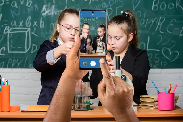 hands holding a smart phone capturing an image of two young students in a classroom