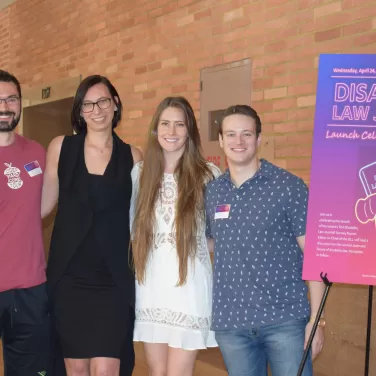 Four UCLA Law students posing next to the Disability Law Journal poster